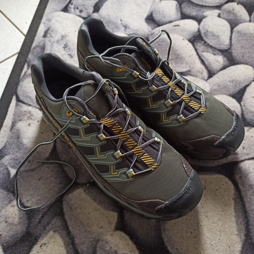 grün-graue Wanderschuhe/Trailrunning-Schuhe auf einem Teppich mit Stein-Muster
